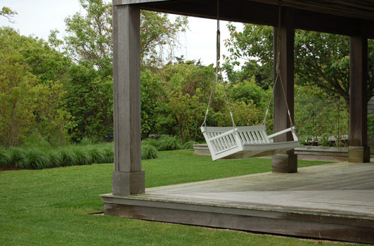 title:A swing was hung at the wraparound porch to enjoy the bird life in the morning garden area.